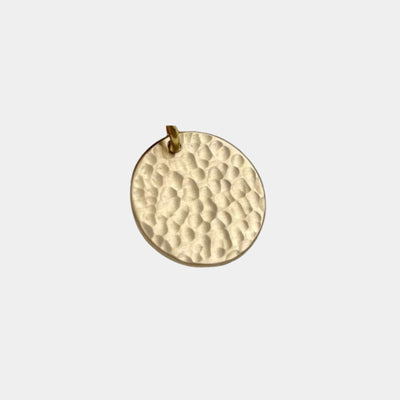 A round hammered metal pendant in a warm gold or brass tone, shown against a plain light gray background.